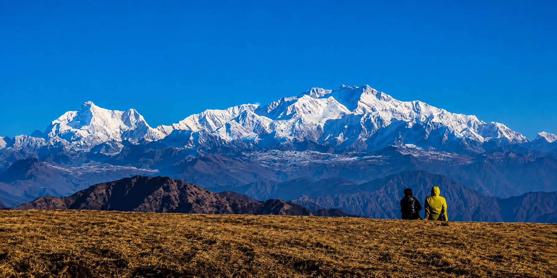 Two trekkers seated on the Singalila Ridge looking at the Kanchenjunga massif